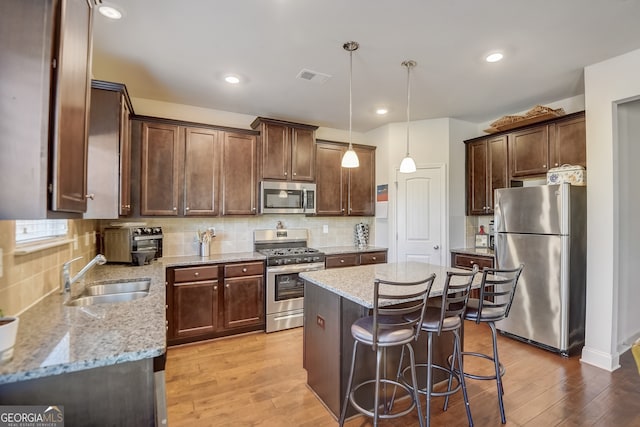 kitchen with sink, pendant lighting, appliances with stainless steel finishes, and light hardwood / wood-style flooring