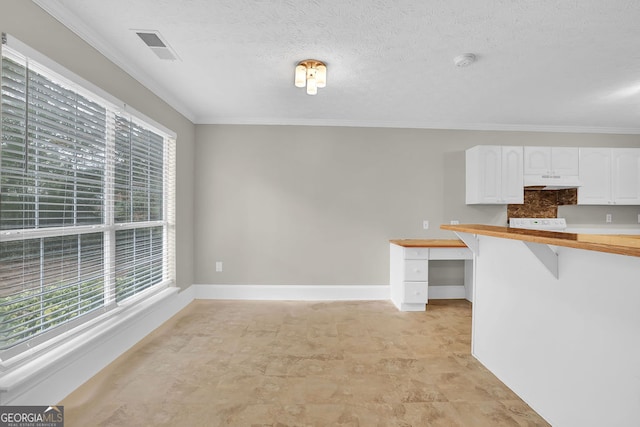 kitchen featuring wooden counters, a textured ceiling, ornamental molding, white cabinetry, and built in desk