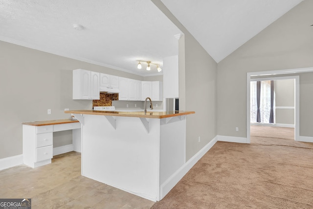 kitchen with white cabinetry, light colored carpet, a kitchen breakfast bar, kitchen peninsula, and lofted ceiling