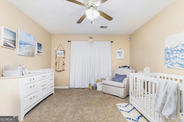 bedroom with a nursery area, a ceiling fan, visible vents, and light colored carpet