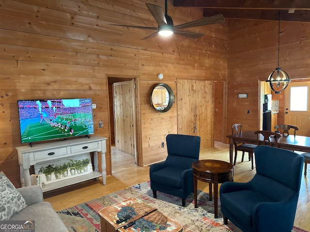 living room with ceiling fan with notable chandelier, light wood-type flooring, high vaulted ceiling, and wood walls