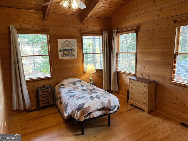 bedroom with ceiling fan, light hardwood / wood-style flooring, wooden walls, and multiple windows