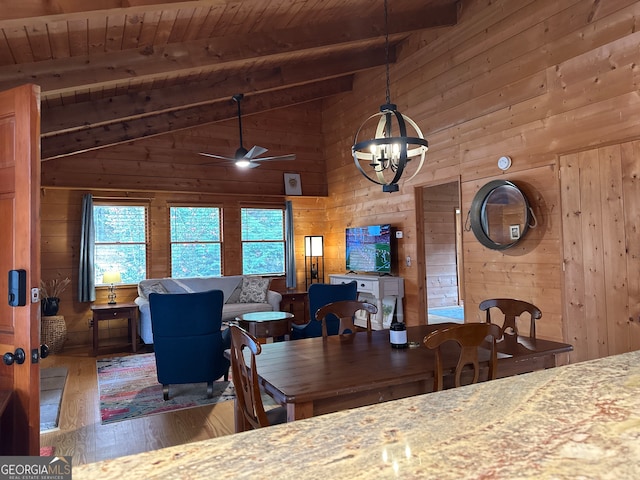 dining area with hardwood / wood-style floors, wood walls, ceiling fan with notable chandelier, beamed ceiling, and wood ceiling