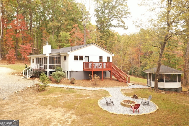 rear view of property featuring a sunroom, a deck, an outdoor fire pit, and a lawn