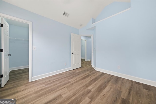 unfurnished bedroom featuring a closet, a walk in closet, hardwood / wood-style floors, and lofted ceiling