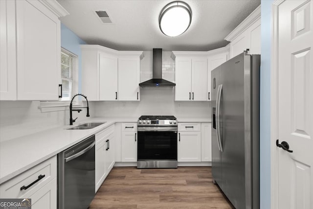 kitchen with stainless steel appliances, light hardwood / wood-style floors, white cabinetry, sink, and wall chimney exhaust hood