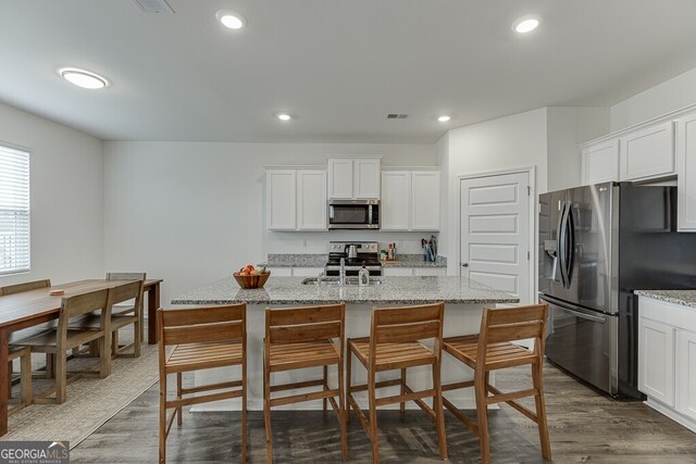 kitchen with dark hardwood / wood-style floors, stainless steel appliances, and an island with sink