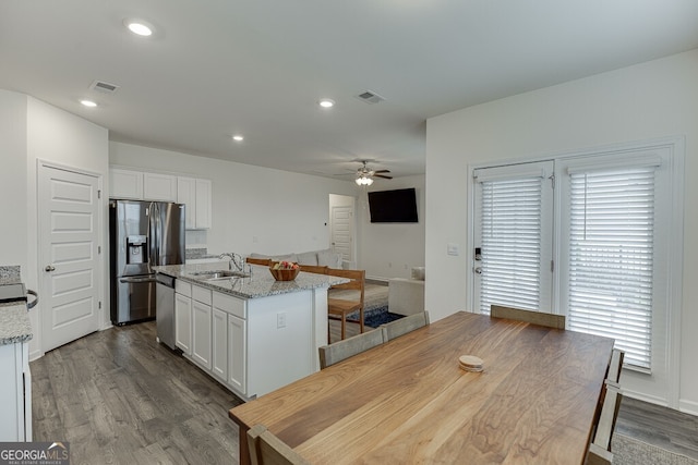 kitchen with a center island with sink, hardwood / wood-style flooring, ceiling fan, light stone counters, and white cabinetry