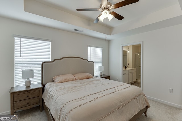 carpeted bedroom with a tray ceiling, ensuite bath, and ceiling fan