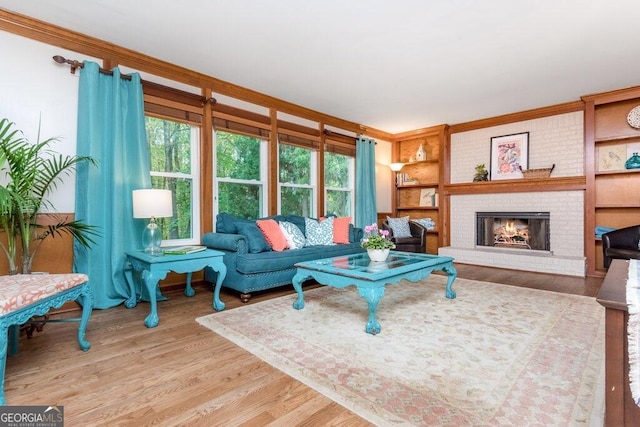 living room with a brick fireplace, light hardwood / wood-style flooring, built in shelves, and crown molding