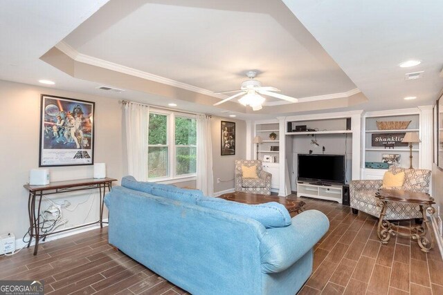 living room featuring dark wood-type flooring, ceiling fan, crown molding, and a tray ceiling