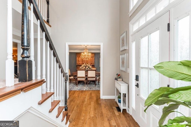 foyer entrance featuring a towering ceiling, light wood-type flooring, crown molding, and an inviting chandelier