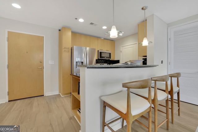 kitchen featuring stainless steel appliances, decorative light fixtures, light brown cabinets, light hardwood / wood-style floors, and kitchen peninsula