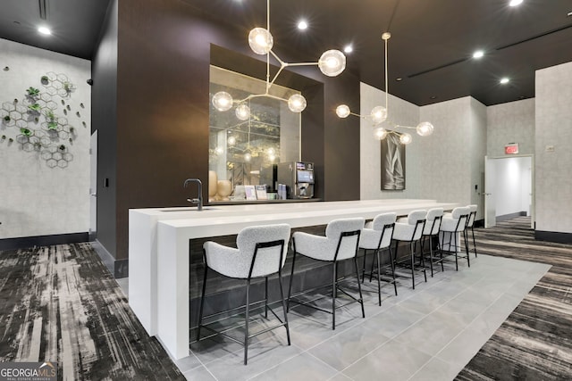 bar featuring light tile patterned floors, a high ceiling, sink, and decorative light fixtures