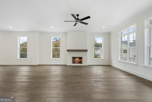 unfurnished living room featuring dark wood-type flooring, a wealth of natural light, and ornamental molding