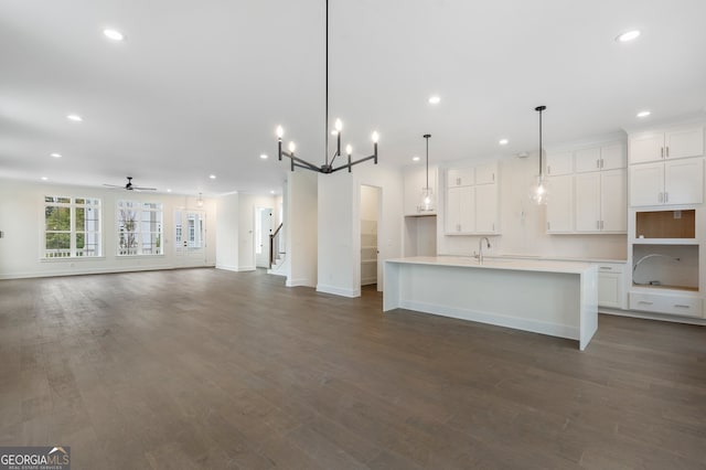 kitchen with white cabinetry, ceiling fan with notable chandelier, decorative light fixtures, an island with sink, and dark hardwood / wood-style flooring