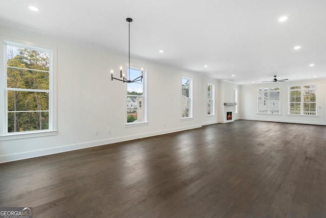 unfurnished living room with ornamental molding, dark hardwood / wood-style floors, and ceiling fan with notable chandelier