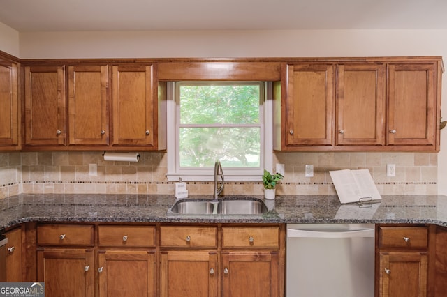 kitchen featuring dark stone counters, decorative backsplash, stainless steel dishwasher, and sink