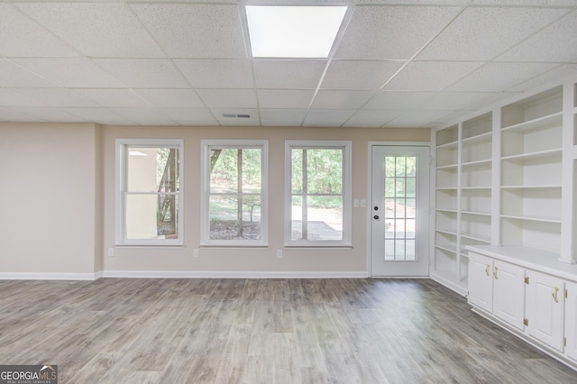 empty room with built in features, light wood-type flooring, and a drop ceiling