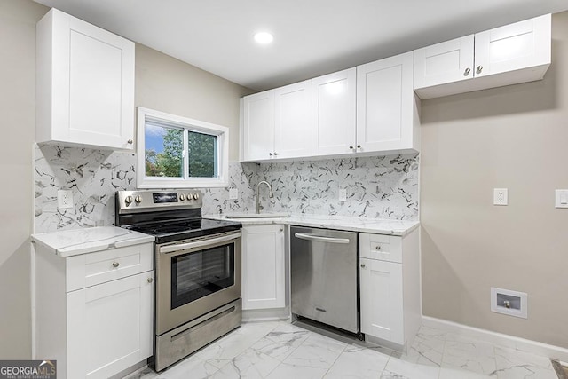 kitchen featuring marble finish floor, stainless steel appliances, white cabinetry, a sink, and baseboards