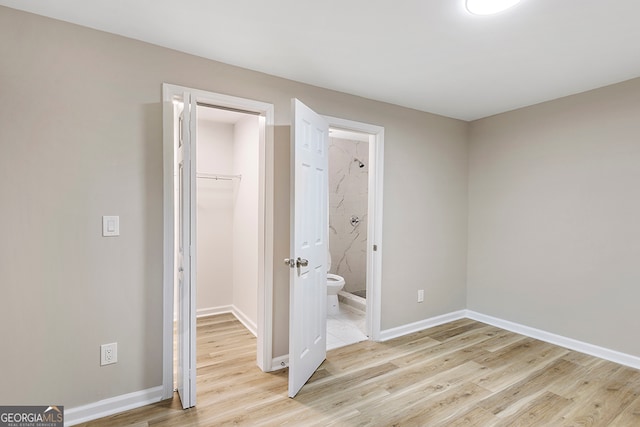 unfurnished bedroom featuring ensuite bathroom, light hardwood / wood-style flooring, a spacious closet, and a closet