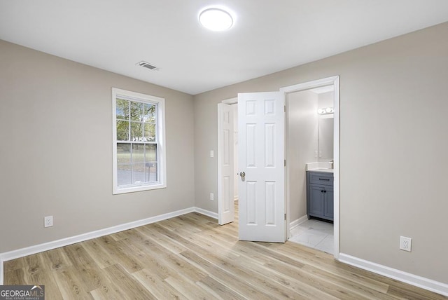 unfurnished bedroom featuring baseboards, visible vents, ensuite bath, and light wood finished floors