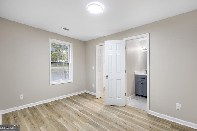 unfurnished bedroom featuring light wood-type flooring, baseboards, and ensuite bathroom