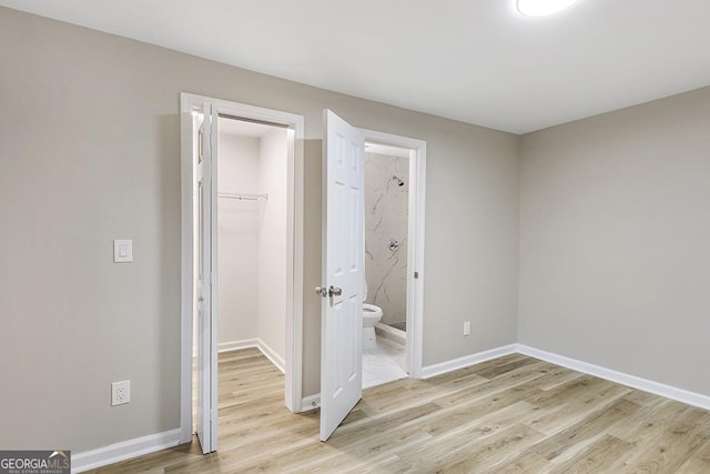 unfurnished bedroom with light wood-type flooring, a walk in closet, baseboards, a closet, and connected bathroom