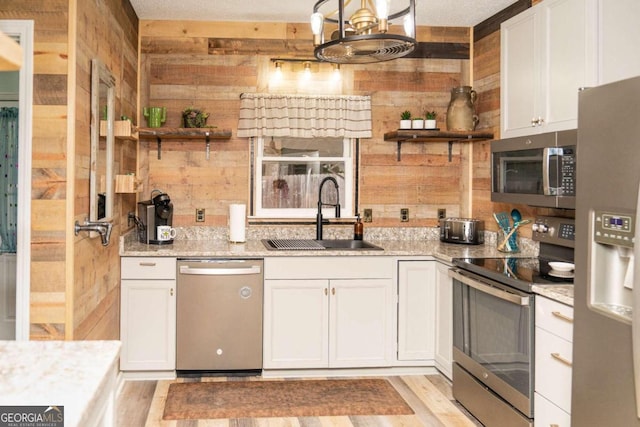 kitchen with sink, white cabinetry, light stone counters, wooden walls, and stainless steel appliances