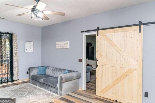 interior space with hardwood / wood-style flooring, a textured ceiling, a barn door, and ceiling fan