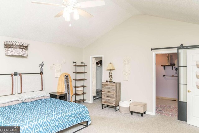 carpeted bedroom with a walk in closet, a barn door, lofted ceiling, and a textured ceiling