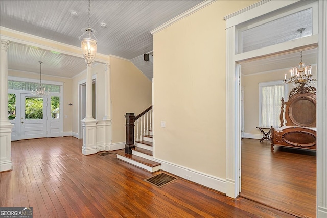 foyer featuring hardwood / wood-style floors, ornate columns, an inviting chandelier, and crown molding