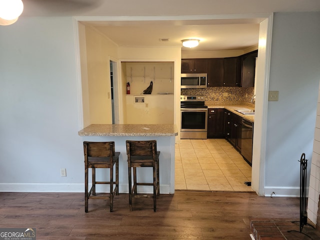 kitchen featuring a kitchen breakfast bar, dark brown cabinetry, stainless steel appliances, and light hardwood / wood-style flooring