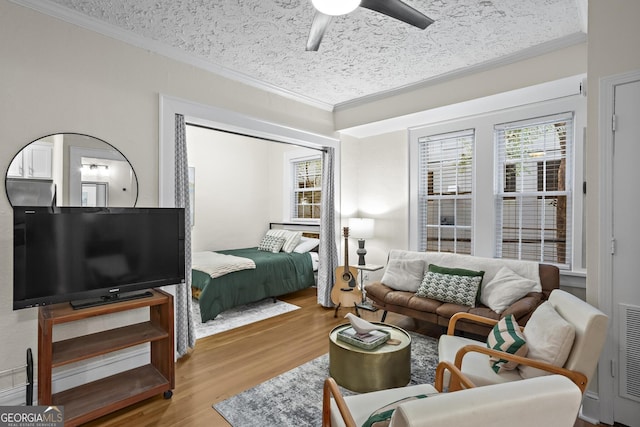 bedroom featuring a textured ceiling, light hardwood / wood-style flooring, ornamental molding, and ceiling fan