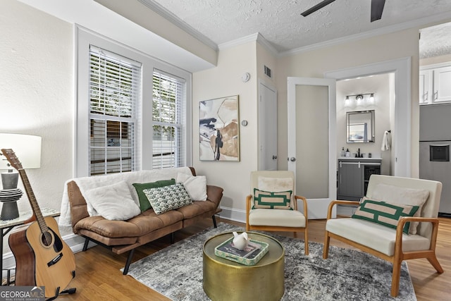 living room with ceiling fan, a textured ceiling, light wood-type flooring, and ornamental molding