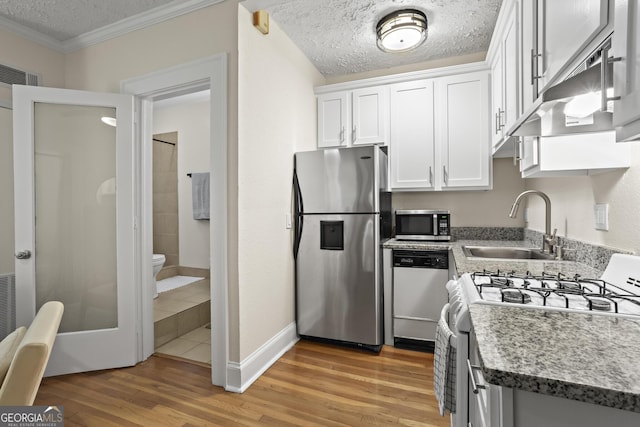 kitchen featuring appliances with stainless steel finishes, a textured ceiling, sink, white cabinets, and light hardwood / wood-style flooring