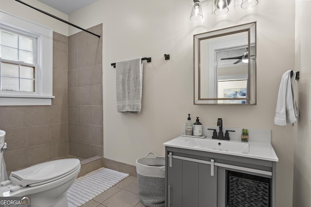 bathroom featuring toilet, tile patterned flooring, a tile shower, vanity, and ceiling fan