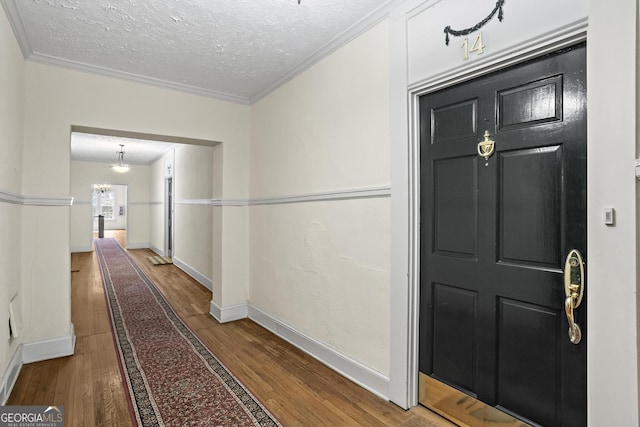 hall with hardwood / wood-style flooring, a textured ceiling, an inviting chandelier, and ornamental molding