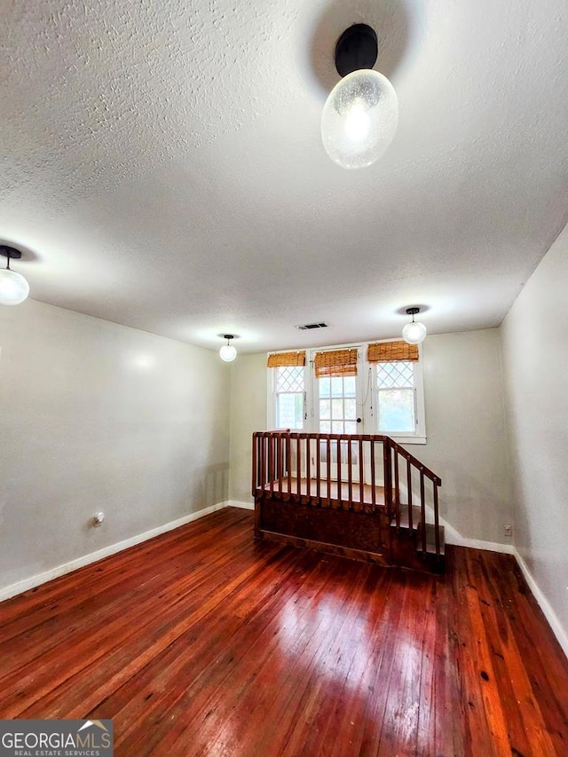 unfurnished room with a textured ceiling and dark hardwood / wood-style floors