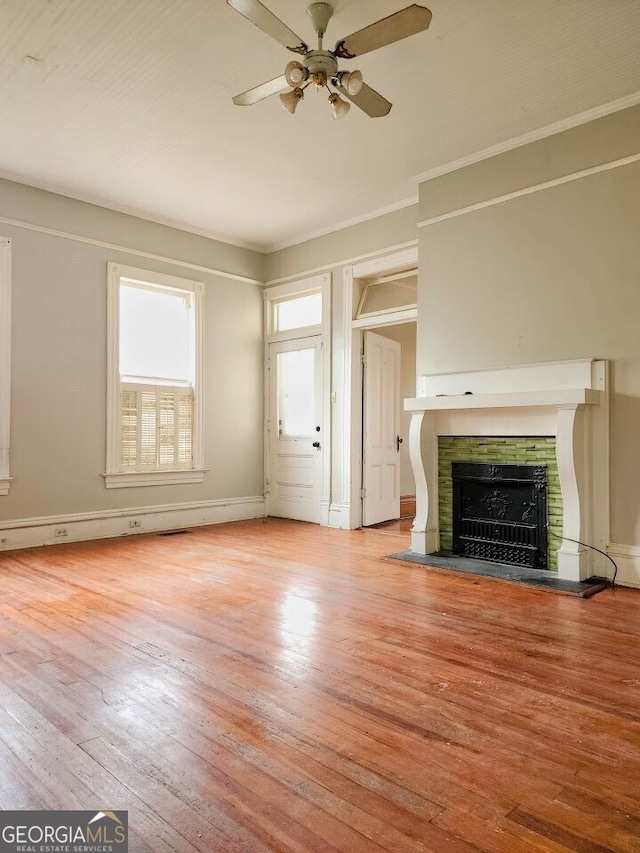 unfurnished living room featuring ornamental molding, light wood-type flooring, ceiling fan, and a tile fireplace