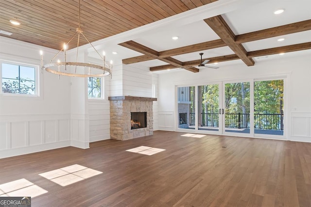 unfurnished living room with dark wood-type flooring, a stone fireplace, beamed ceiling, and ceiling fan with notable chandelier