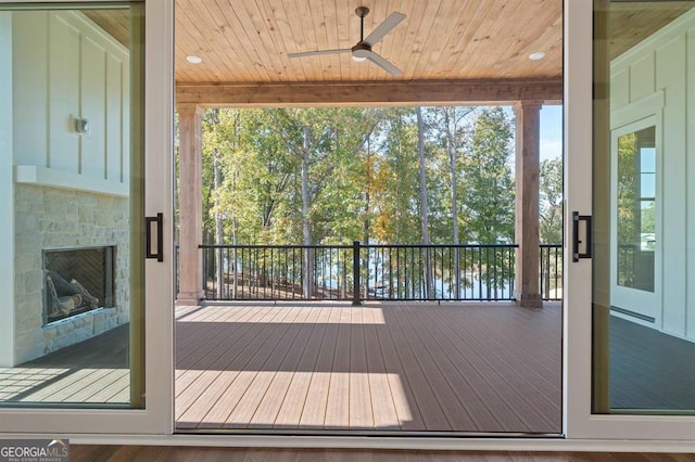 wooden terrace featuring ceiling fan, a tile fireplace, and a water view