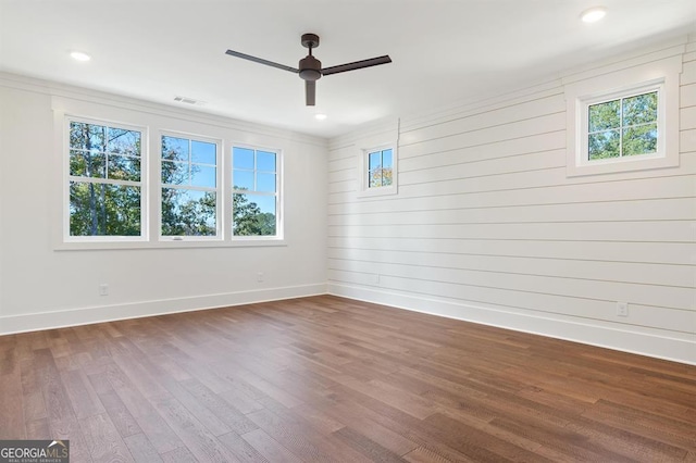 unfurnished room with plenty of natural light, wood walls, dark hardwood / wood-style floors, and ceiling fan