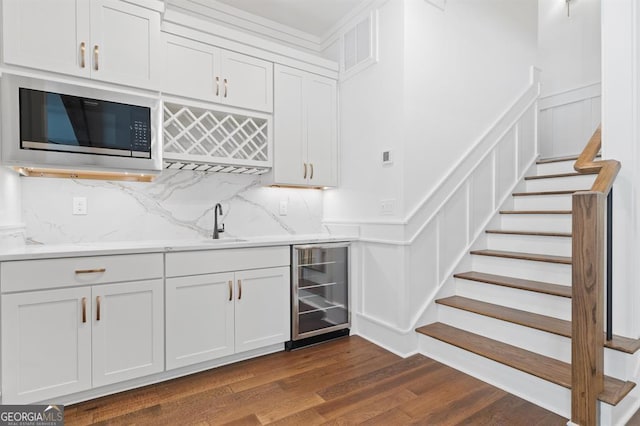 bar with tasteful backsplash, wine cooler, white cabinets, dark wood-type flooring, and stainless steel microwave