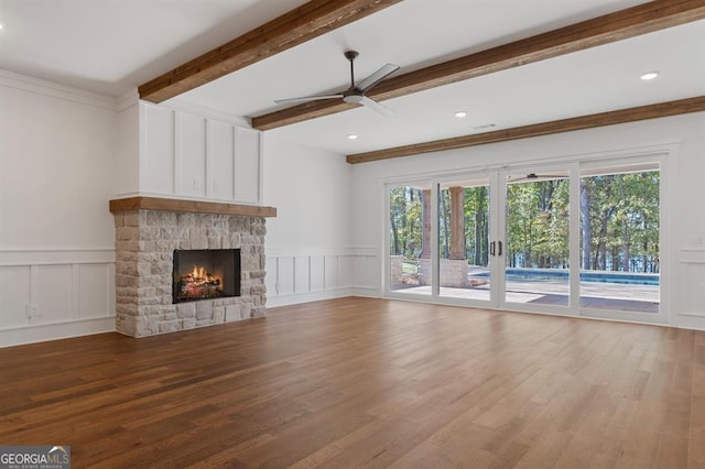 unfurnished living room with a stone fireplace, wood-type flooring, beamed ceiling, ceiling fan, and crown molding