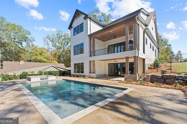 back of house with a balcony, ceiling fan, a patio, and a swimming pool with hot tub