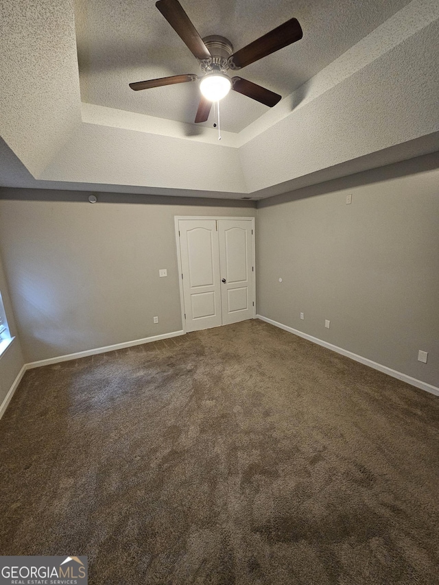 unfurnished bedroom with a tray ceiling, carpet flooring, baseboards, and a textured ceiling