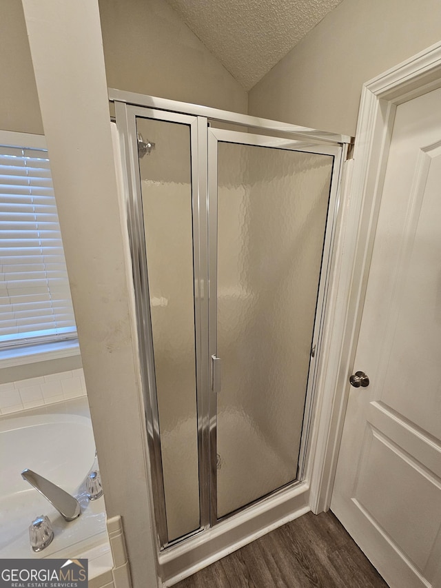 bathroom with wood finished floors, lofted ceiling, a stall shower, a textured ceiling, and a garden tub