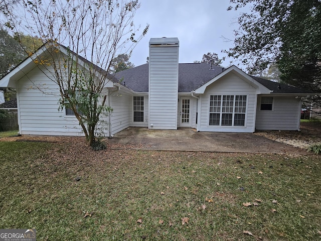 rear view of property featuring a lawn, roof with shingles, a chimney, and a patio area