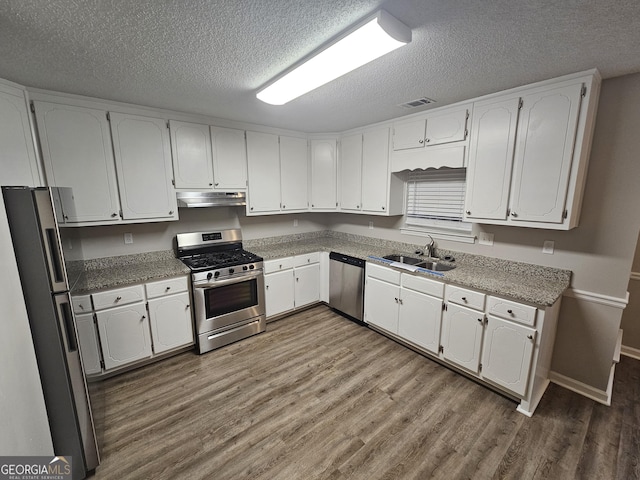 kitchen featuring under cabinet range hood, a sink, wood finished floors, white cabinetry, and appliances with stainless steel finishes